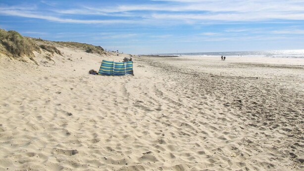 Ein Strand mit einem gestreiften Strandsonnenschirm und einem Zelt.