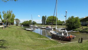 Ein ruhiger Fluss mit vertäuten Booten entlang des Ufers, umgeben von Wiesen und Bäumen.