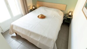 Un lit bien fait, recouvert d’une courtepointe blanche, un chapeau de paille posé sur le lit et deux lampes de chevet sur les tables de nuit.