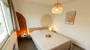 A neatly arranged hotel room with a bed, a bedside lamp, a wall-mounted lamp, a map, and a window with curtains.