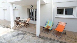 Un bâtiment blanc doté d’un patio couvert comprenant une table, des chaises, une horloge et une fenêtre.