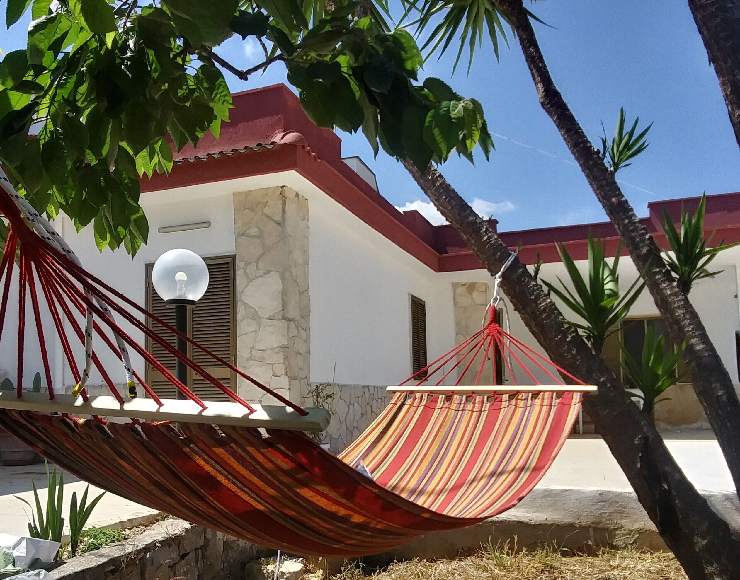 A hammock under a tree, a stone wall, and a building with a red roof.