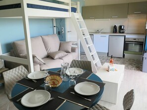 A room with a bunk bed, a dining table set with plates and glasses, a coffee machine, and a refrigerator.