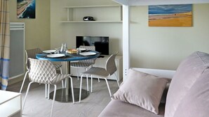 Ett modernt vardagsrum med ett runt matbord, vita stolar, en platt-TV och en soffa med kuddar.