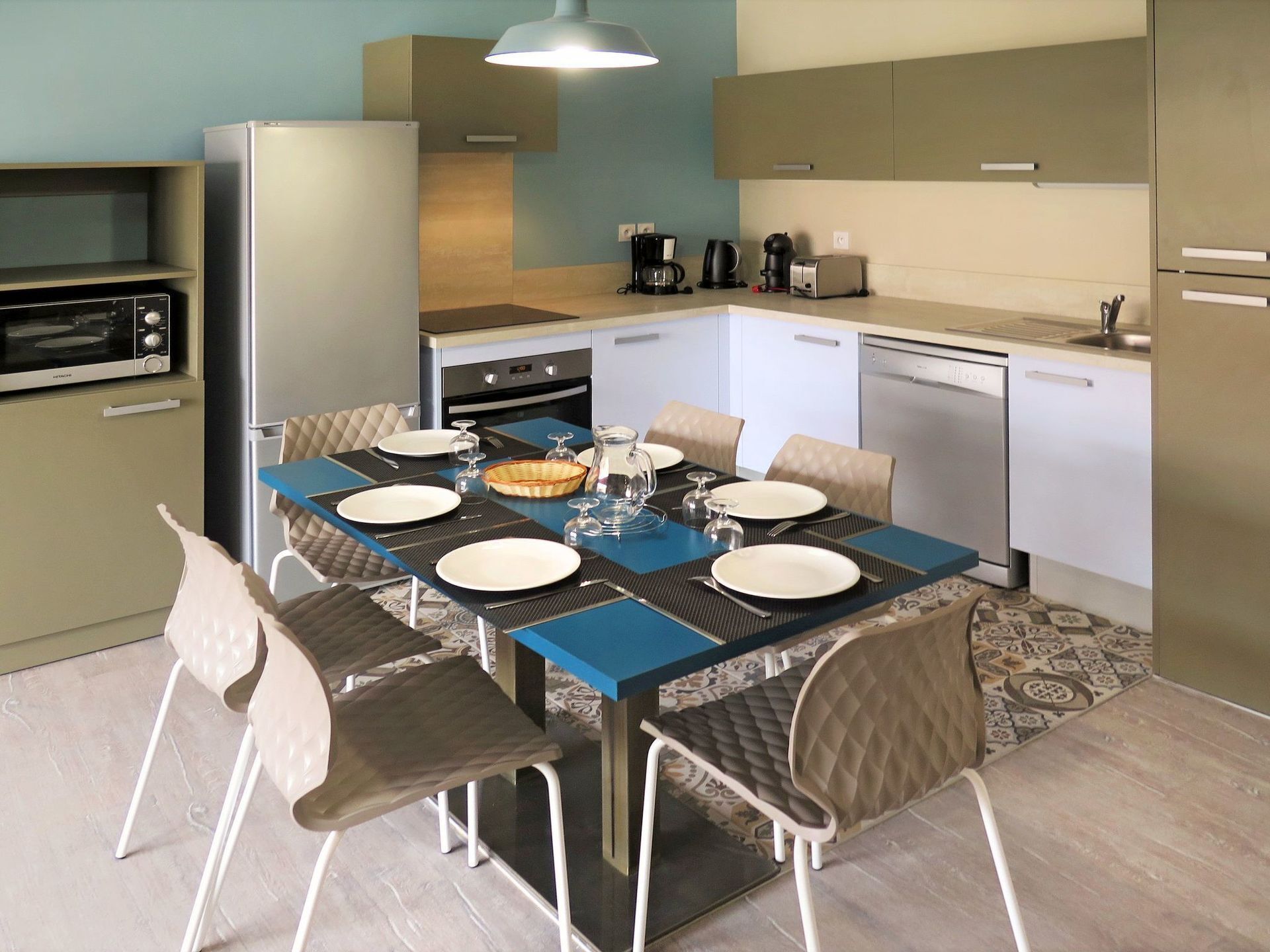 A compact kitchen with a dining table set for six, equipped with basic appliances and a coffee maker.