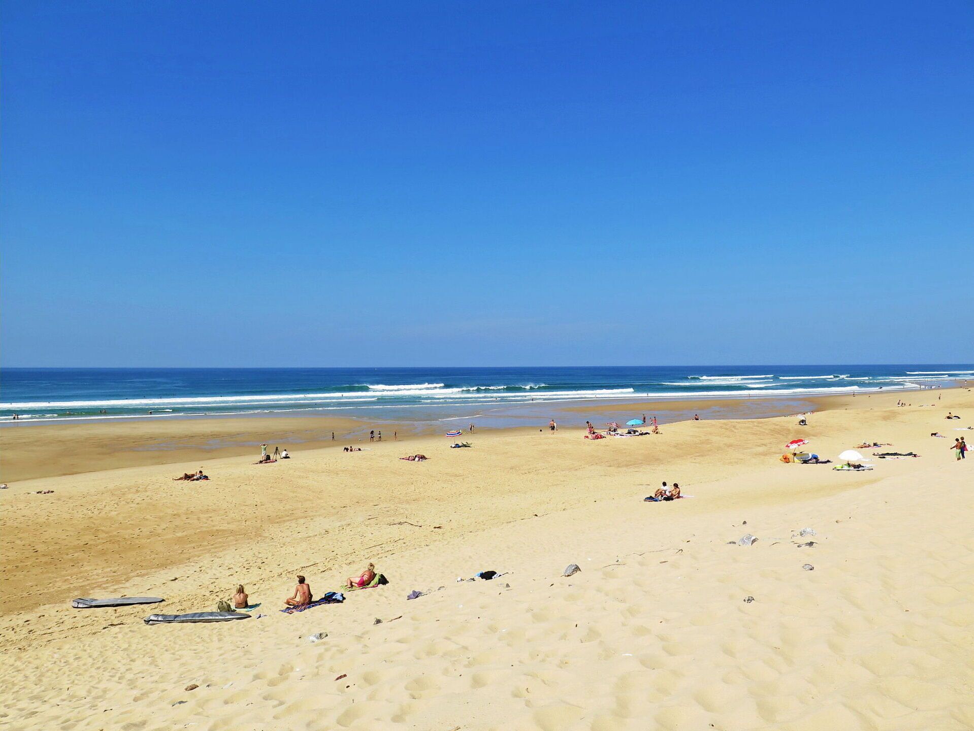 Una extensa playa de arena con gente tomando el sol y nadando.