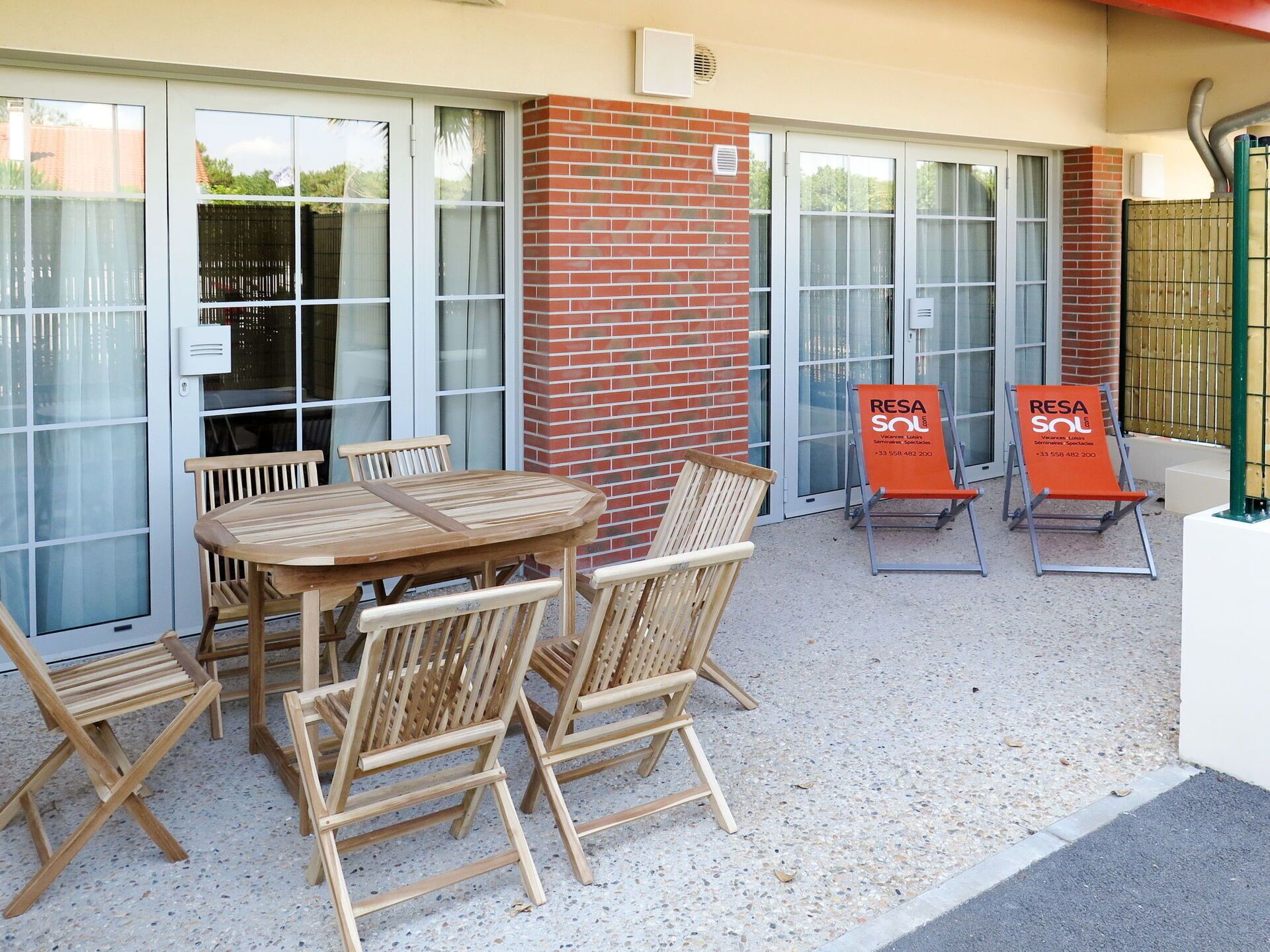 Un espacio al aire libre con mesa y sillas de madera, una pared de ladrillo y un acceso por puerta de cristal.