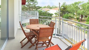 Ein Balkon mit Holztisch und -stühlen, einer Glastür und Blick auf Grünflächen und Gebäude.