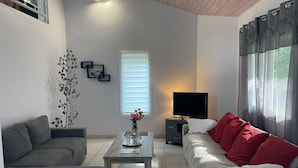 Uma sala de estar com sofá, mesa de centro, televisão e janela com persianas.
