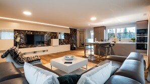 Een moderne woonkamer met een bank, salontafel en televisie. Een keuken is zichtbaar op de achtergrond.