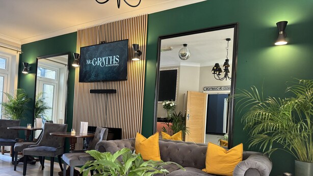 A modern lounge area with a grey sofa, yellow cushions, and a large mirror. - McGraths Blackpool (Blackpool)