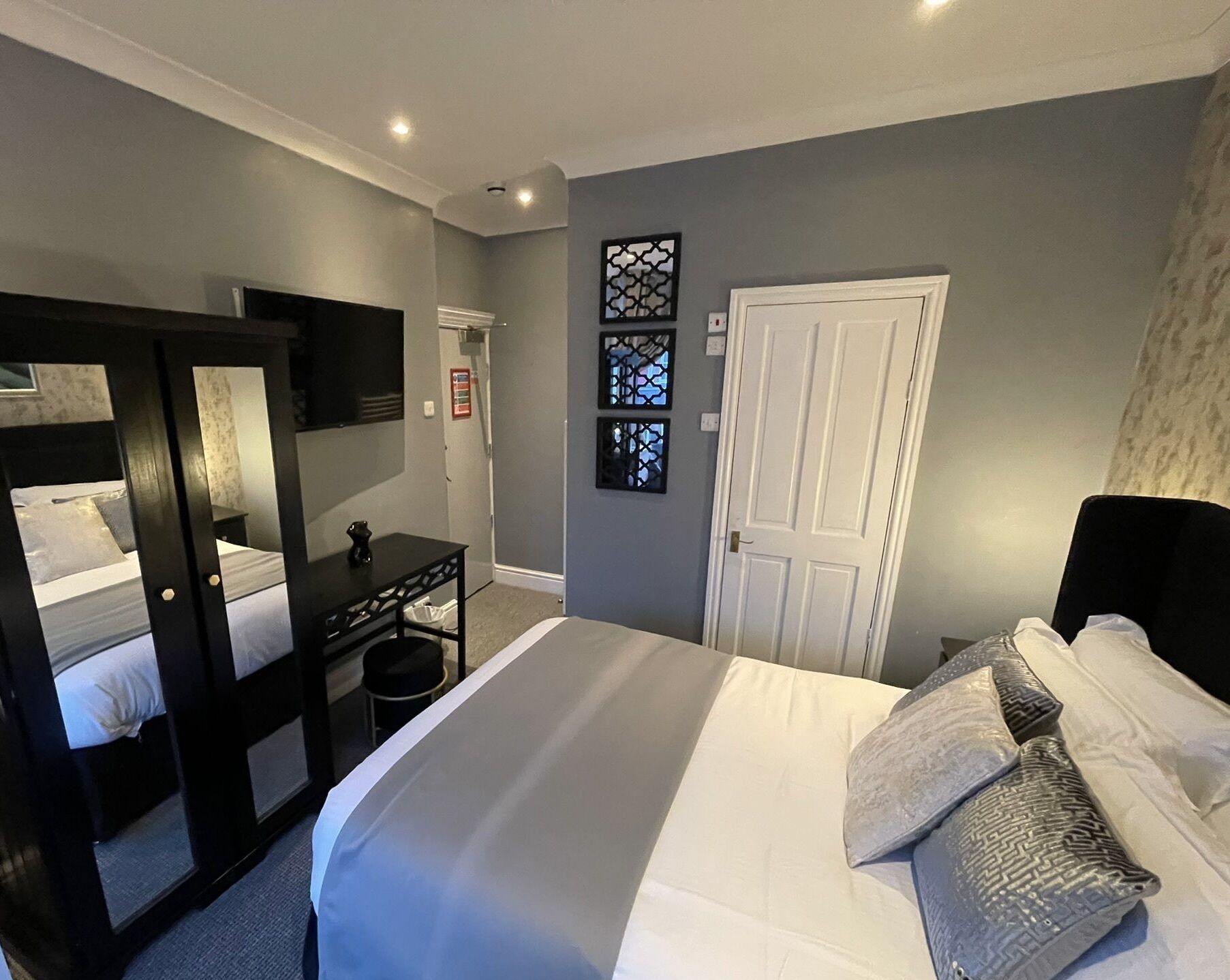 A hotel room with a large bed, a desk, a mirror, and a door.