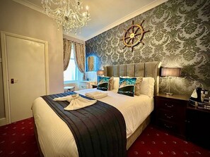 A hotel room with a large bed, a chandelier, a ship's wheel on the wall, and a red carpet. - McGraths Blackpool (Blackpool)