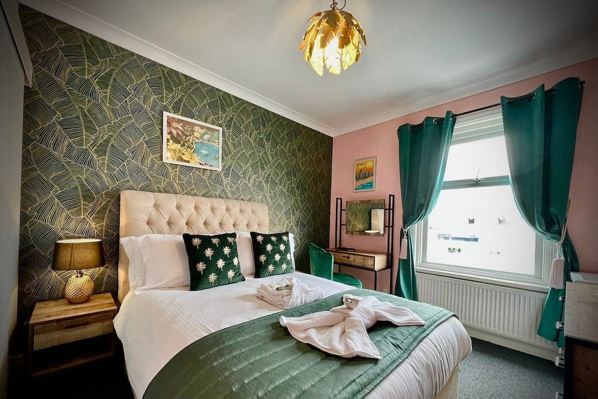 A neatly arranged bedroom with a tufted headboard, a green bedspread, and a decorative lamp on the nightstand.