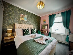 A neatly arranged bedroom with a tufted headboard, a green bedspread, and a decorative lamp on the nightstand. - McGraths Blackpool (Blackpool)