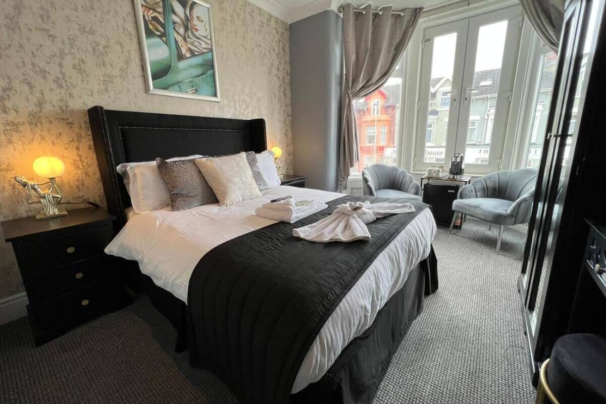 A hotel room with a large bed, a bedside table, a chair, and a view of buildings through the window.