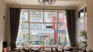 A hotel dining area with tables set for breakfast, large windows with curtains, and a view of the street. - McGraths Blackpool (Blackpool)