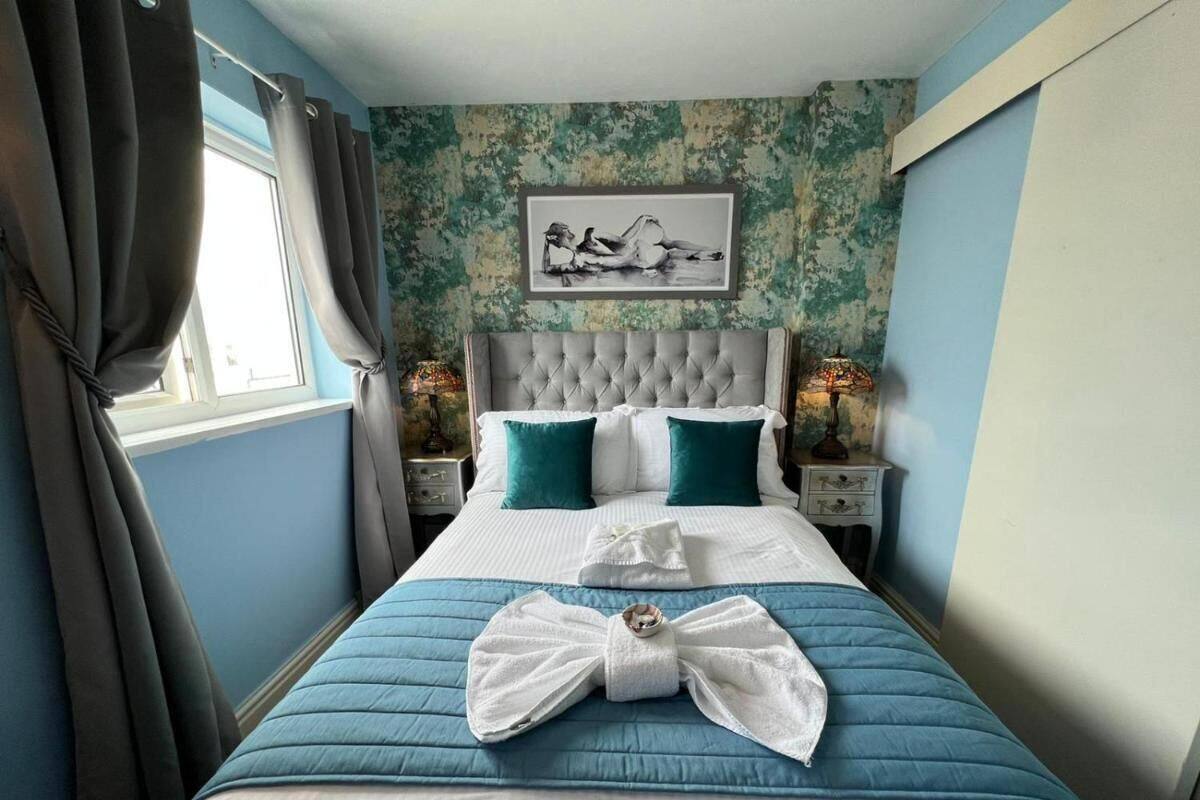 A neatly made bed with a blue quilt, white pillows, and a white towel arranged in a bow on the bed. There is a framed picture on the wall above the bed.