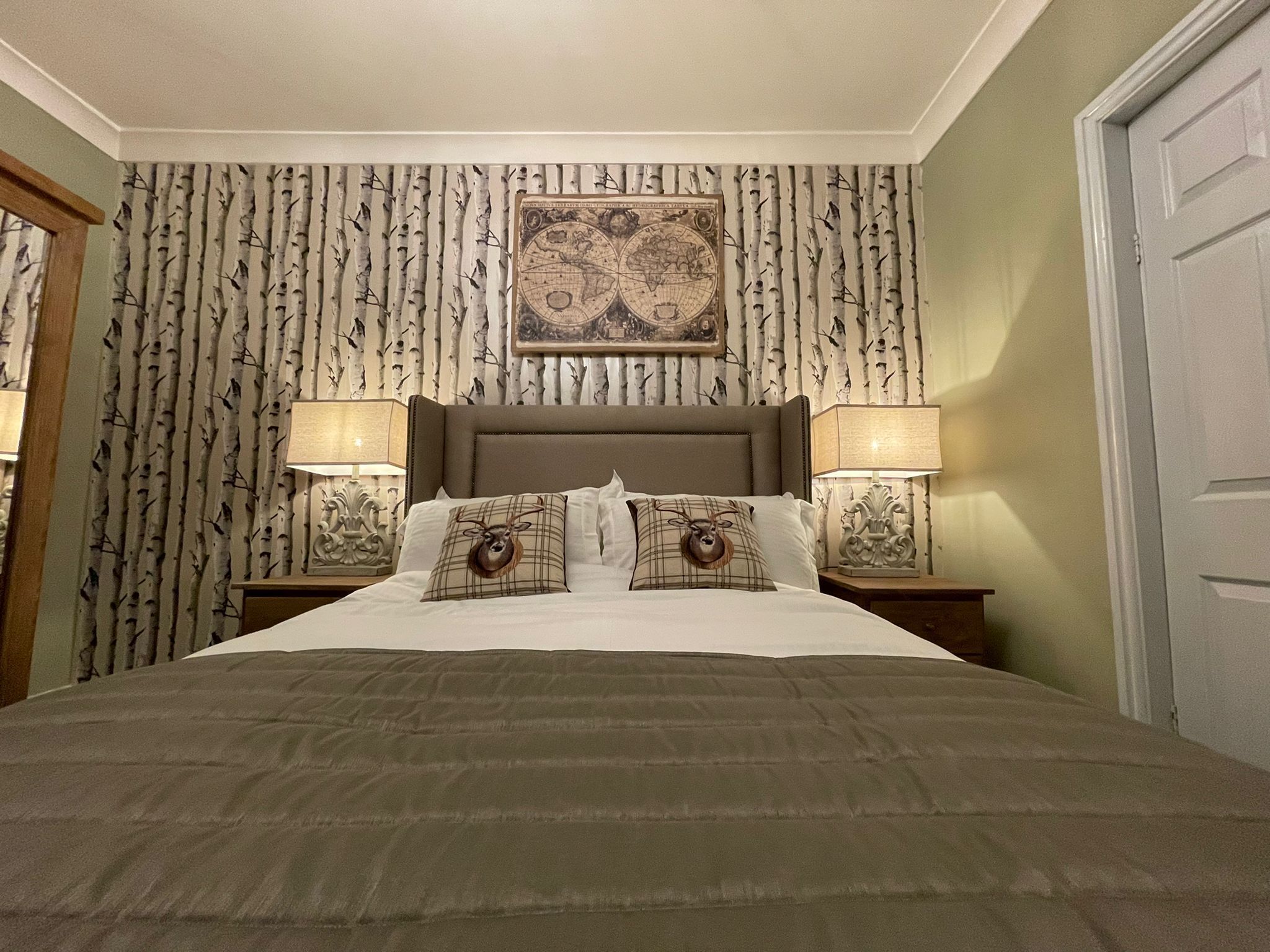 A neatly made bed with a brown headboard, two decorative pillows, and a wall-mounted map.