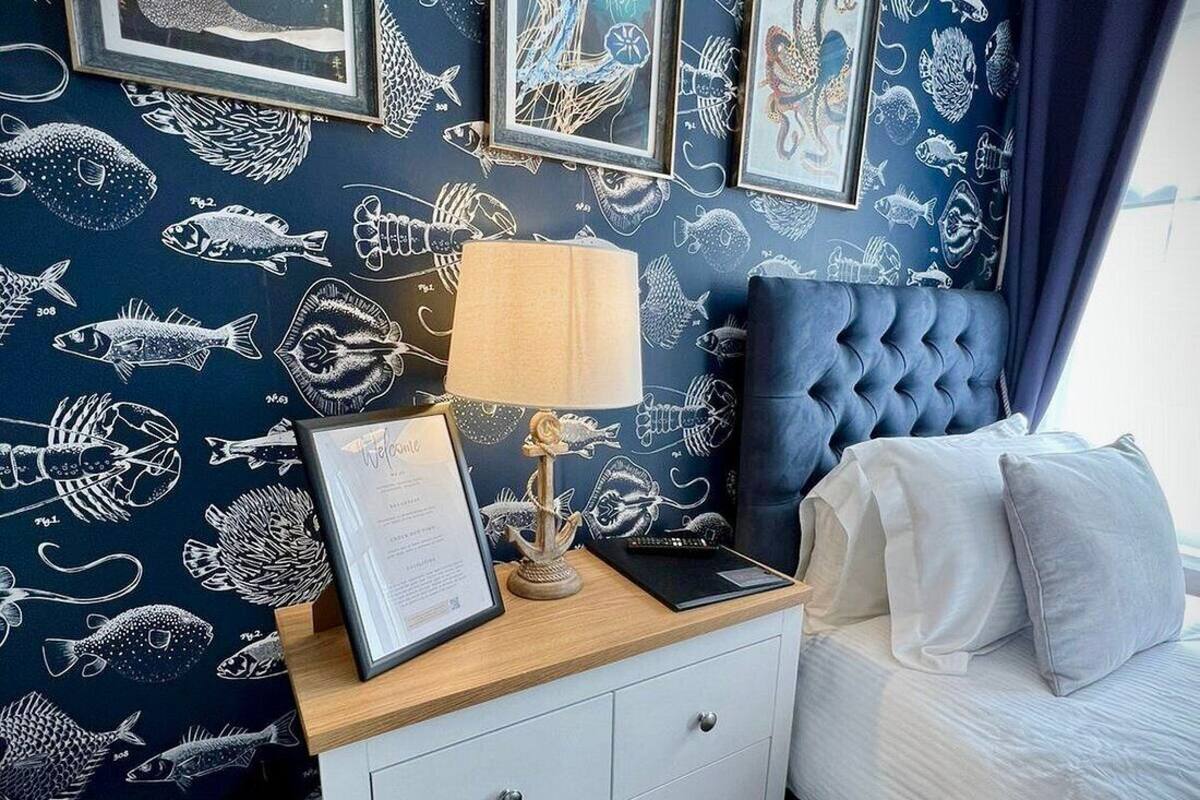 A bedroom with a navy blue wall featuring white fish patterns, a tufted headboard, a bedside table with a lamp, and a framed certificate.