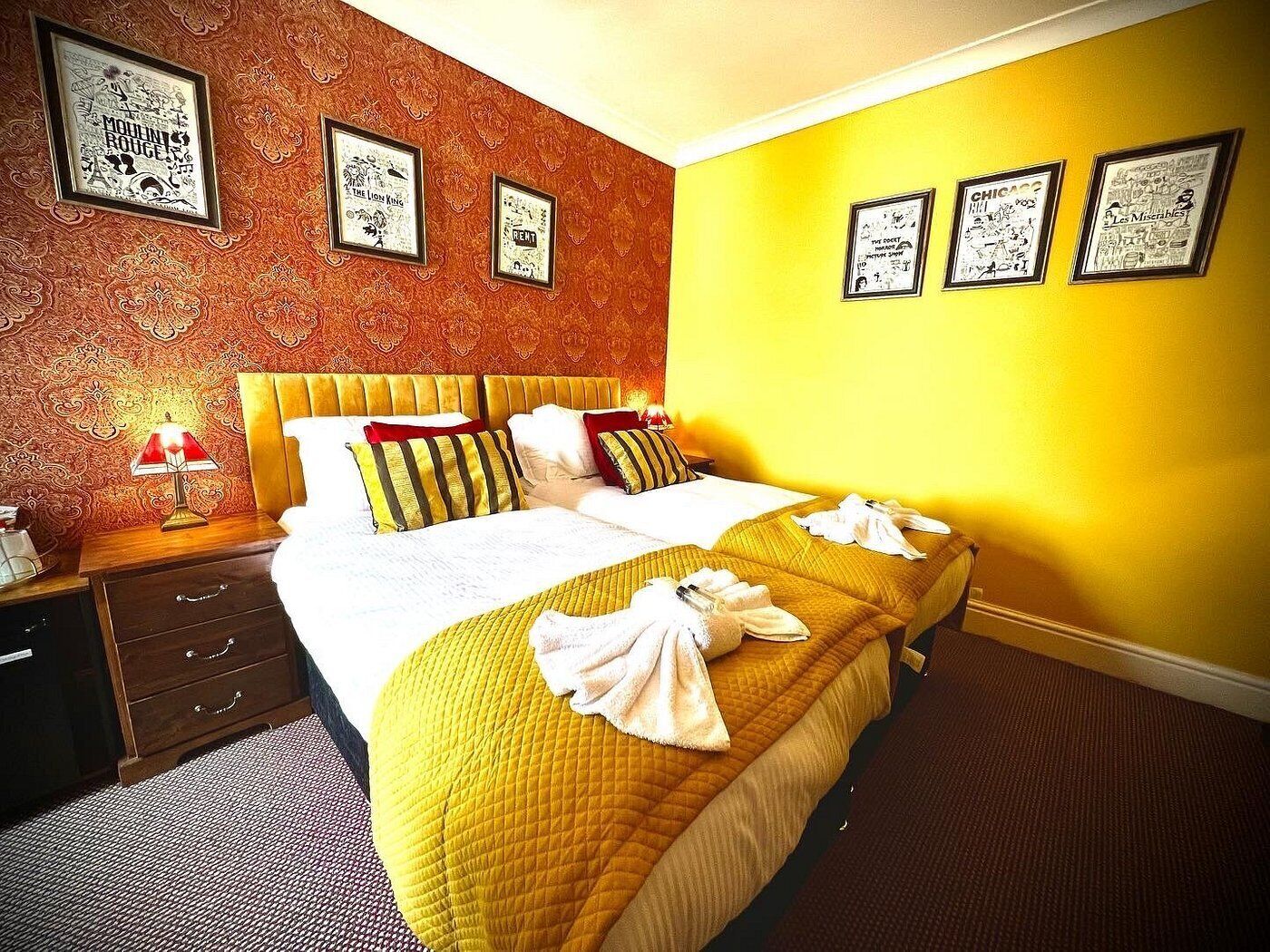 Habitación de hotel con una cama grande, una mesita de noche, una lámpara y cuadros en las paredes.