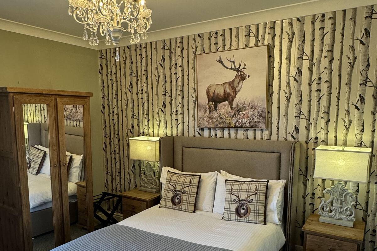 A bedroom with a large bed, a chandelier, and a wall with a tree pattern.