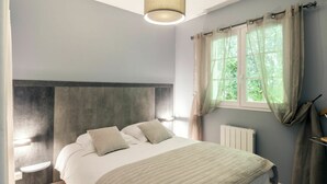 Une chambre à coucher avec un lit, des tables de chevet, une fenêtre avec des rideaux et un radiateur.