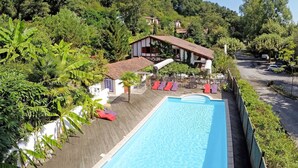 Une piscine entourée de chaises longues, de verdure luxuriante et d’un bâtiment au toit rouge.