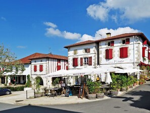 Een restaurant met terras, witte muren, rode luiken en een helderblauwe lucht.
