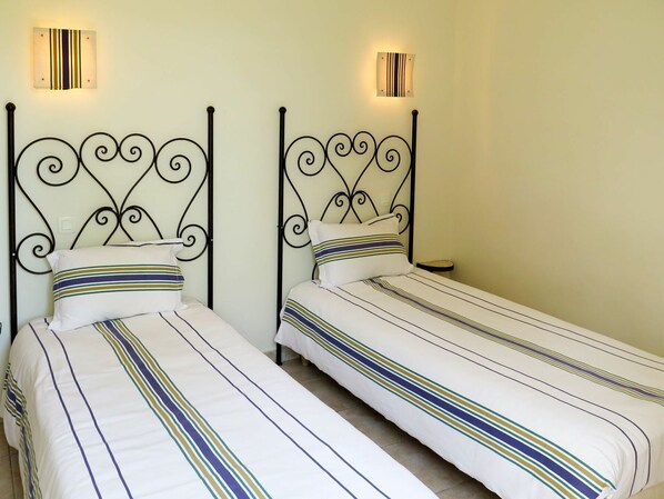 Deux lits simples avec du linge de lit à rayures, un luminaire fixé au mur et une petite table de chevet.