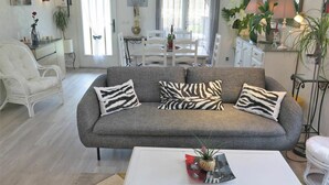 A living room with a grey sofa, white armchairs, and a dining area with a white table and chairs. - Wonderful private villa for 4 guests with private pool, WIFI, TV, terrace and pets allowed (Labenne)