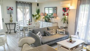 A modern living room with a grey sofa, white chairs, a dining table with fruit, and a white coffee table. - Wonderful private villa for 4 guests with private pool, WIFI, TV, terrace and pets allowed (Labenne)