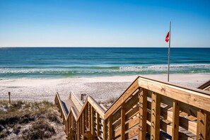 Eine hölzerne Strandpromenade mit einer Flagge, mit Blick auf einen Strand mit Wellen und blauem Himmel.