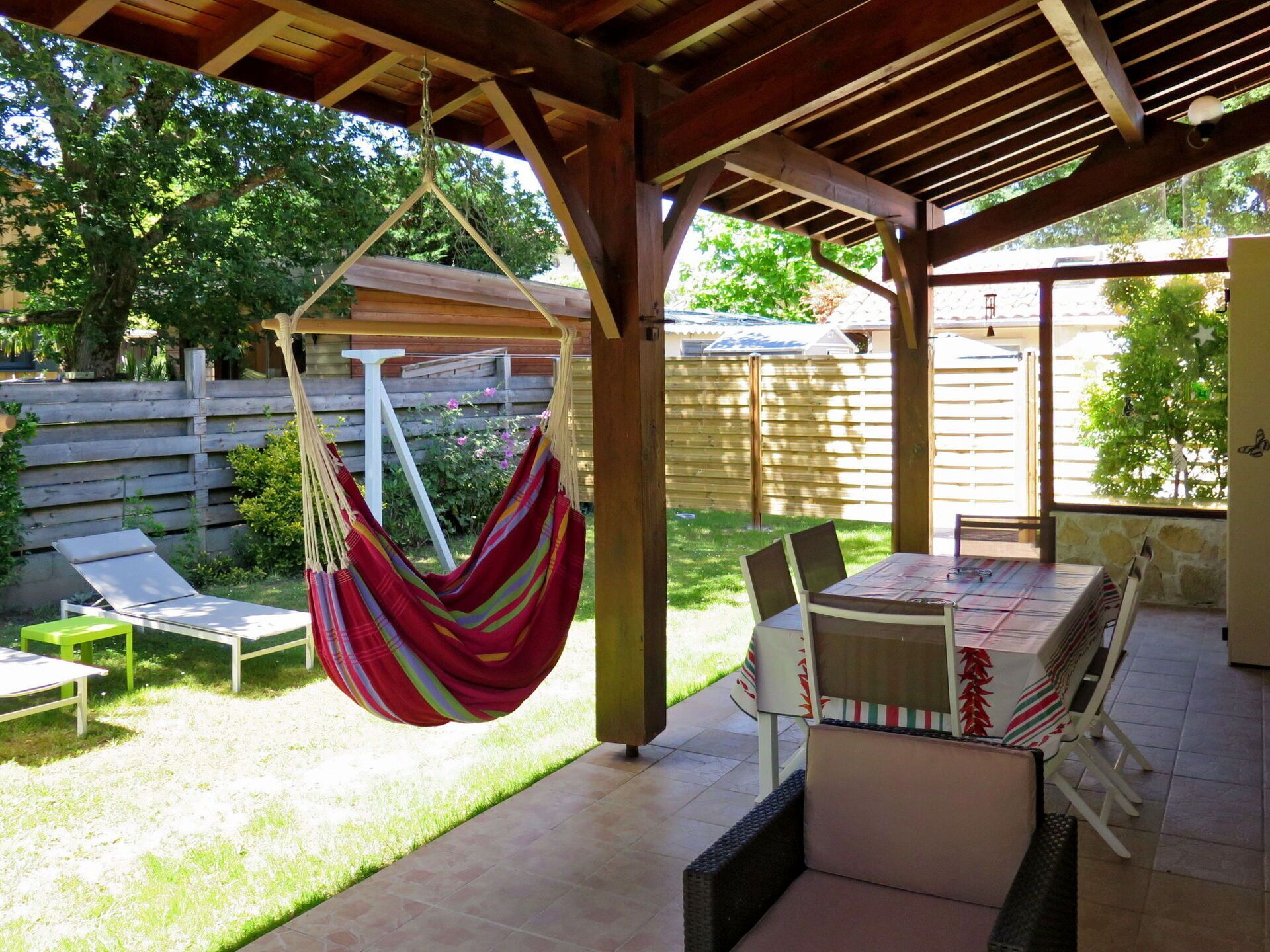 Un patio al aire libre techado con una hamaca, una mesa con sillas y una silla de jardín.