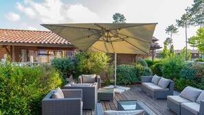 Ein möblierter Patio mit Korbmöbeln, einem großen Sonnenschirm und üppiger Bepflanzung.