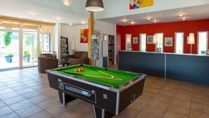 Ein Billardtisch in einem Raum mit roter Wand, einem Empfangstresen und einem Bücherregal.