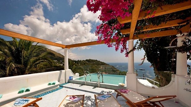 En pool på taget med liggestole, havudsigt og et pergola overdækket med blomster.