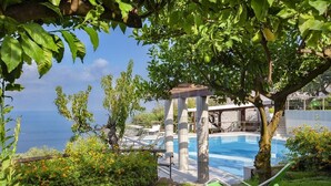 Ein Poolbereich mit einer Pergola, Liegestühlen und Blick aufs Meer.