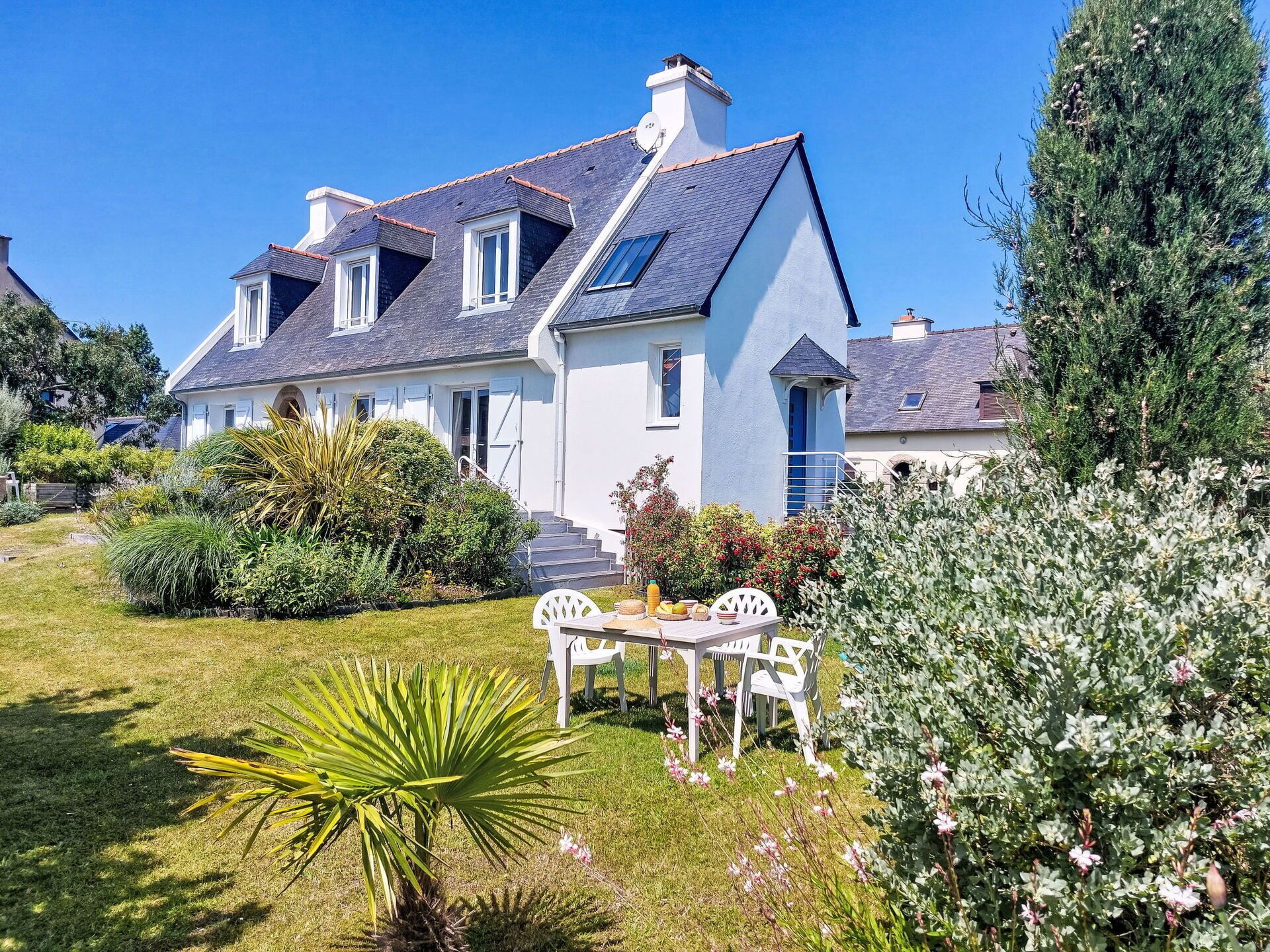 A large house with a sloped roof, a well-maintained garden, and a patio with outdoor furniture.