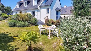 A large house with a sloped roof, a well-maintained garden, and a patio with outdoor furniture. - Nice apartment for 3 guests with WIFI and TV (Cancale)
