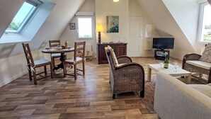 A spacious loft apartment with a high ceiling, wooden flooring, a dining area with chairs, a sofa, a television, and a large window providing natural light. - Nice apartment for 3 guests with WIFI and TV (Cancale)