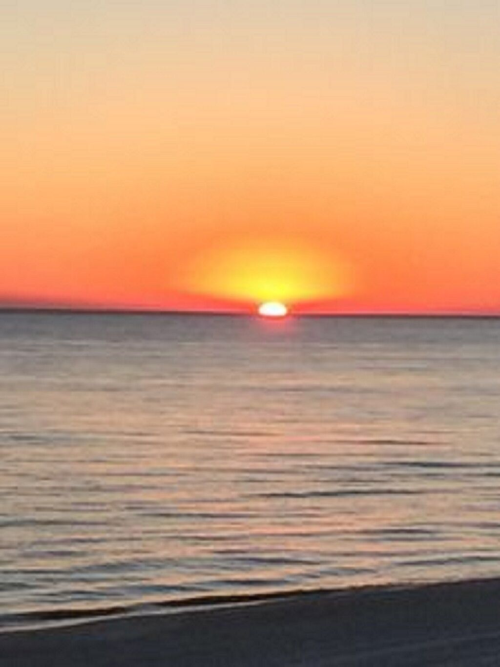 Tramonto su un mare calmo con un orizzonte limpido.