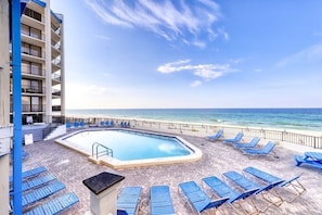 A pool area with lounge chairs and a view of the ocean.