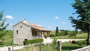 A stone house with a tiled roof, a wooden porch, and a stone wall surrounding the property. - Wonderful private villa for 4 guests with TV, terrace and pets allowed (Labastide-de-penne)