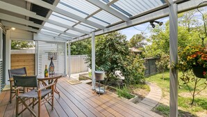Eine überdachte Terrasse mit Holzdeck, Gartenmöbeln und einem Gartenbereich.