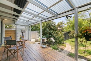 A covered patio with a wooden deck, outdoor seating, and a garden area. - The Beach House Anglesea (Anglesea)