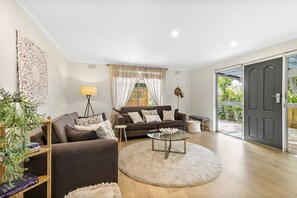 Ein modernes Wohnzimmer mit einem braunen Sofa, einem Glastisch und einem großen Fenster mit Vorhängen.