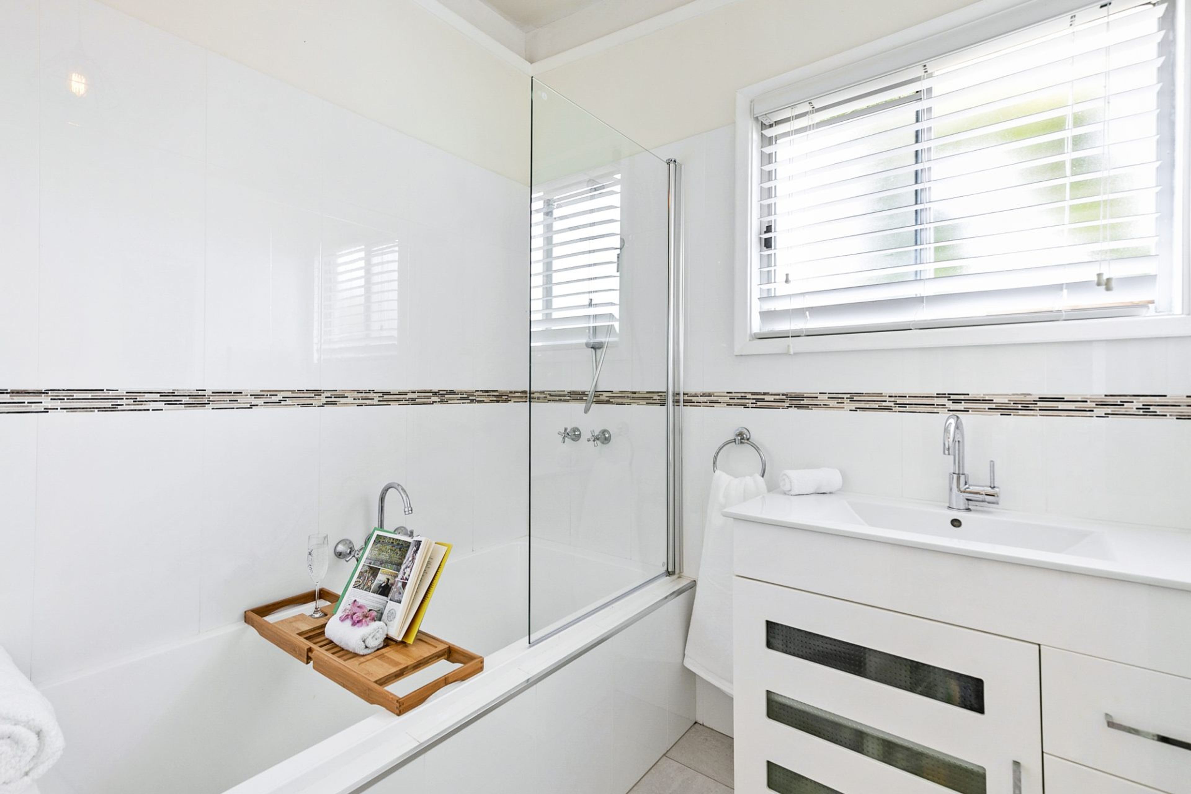 Un baño moderno con cabina de ducha de vidrio, un lavabo blanco y una ventana con persianas.