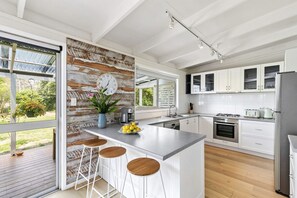 A modern kitchen with a large island, bar stools, a coffee maker, and a clock on the wall. - The Beach House Anglesea (Anglesea)