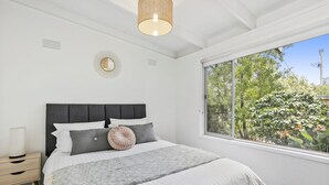 Ein Schlafzimmer mit einem großen Bett, einem Nachttisch, einem wandmontierten Spiegel und einem Fenster mit Blick ins Grüne.